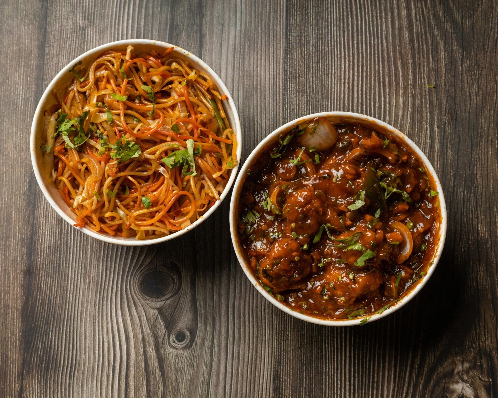 Vibrant bowls of Indo-Chinese noodles and Manchurian on a rustic wooden surface.
