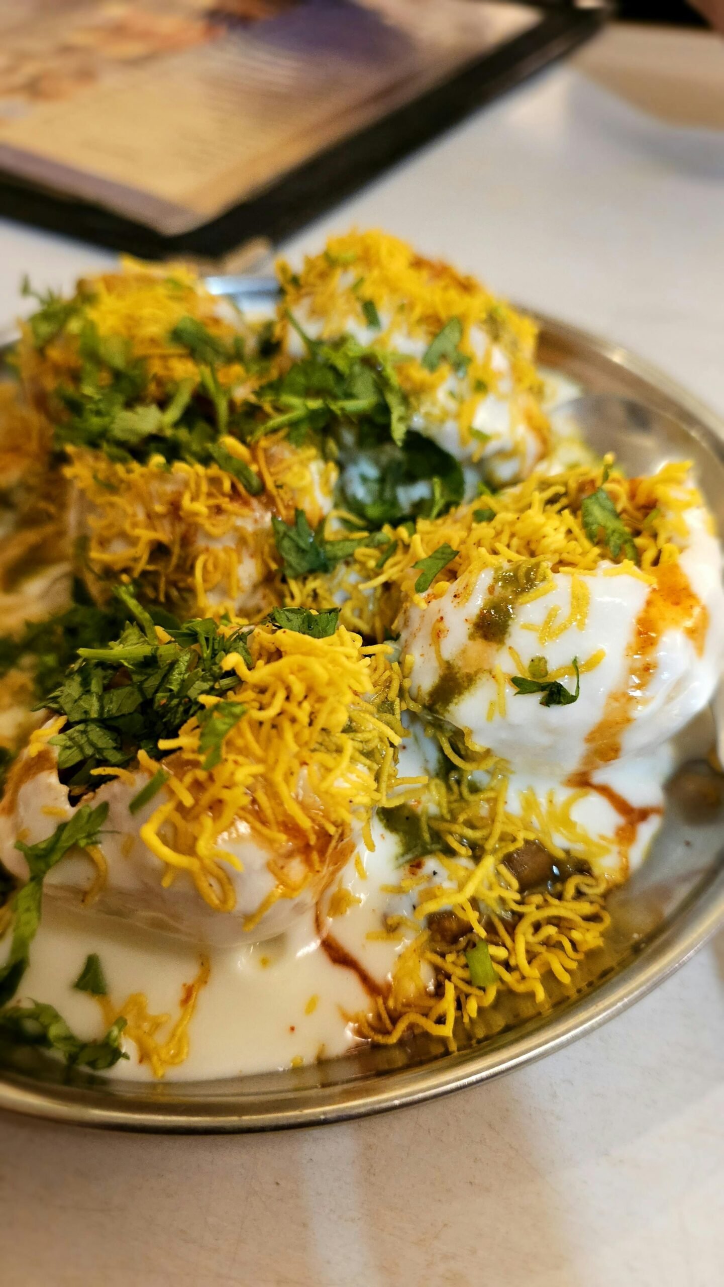 Close-up of Indian Dahi Puri, topped with sev, chutneys, and fresh herbs.